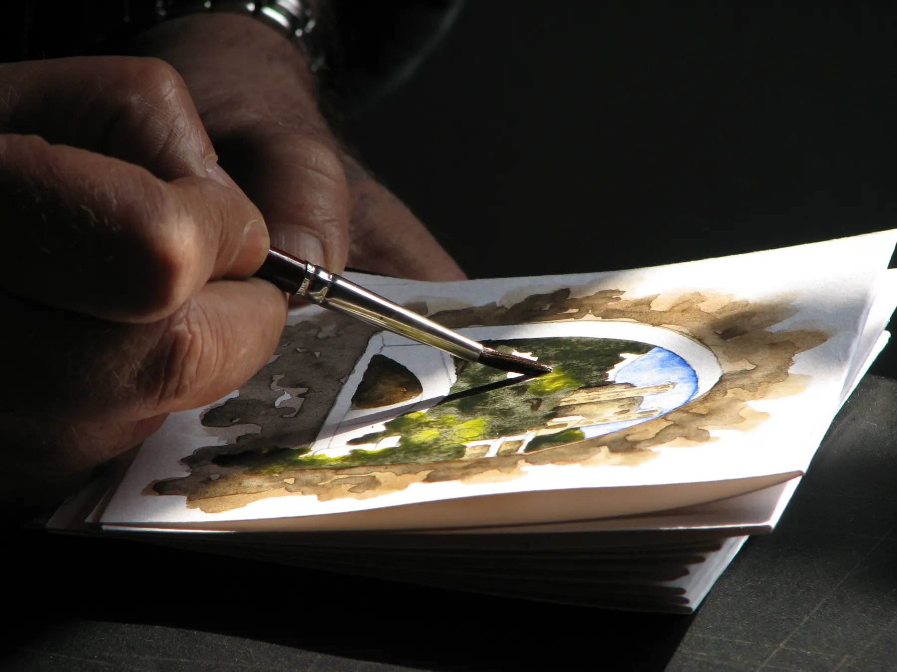 Hands painting a small watercolor study on a block of paper