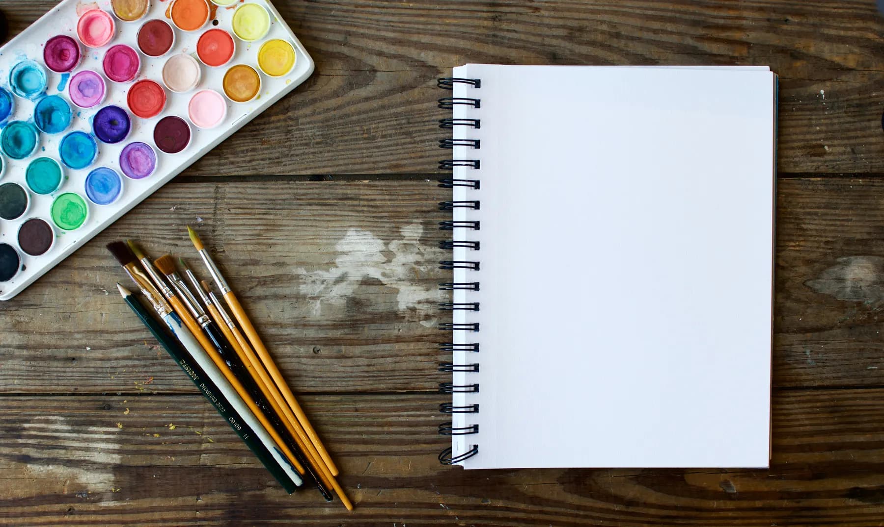 Watercolor brushes laid beside an open sketchbook on a workbench