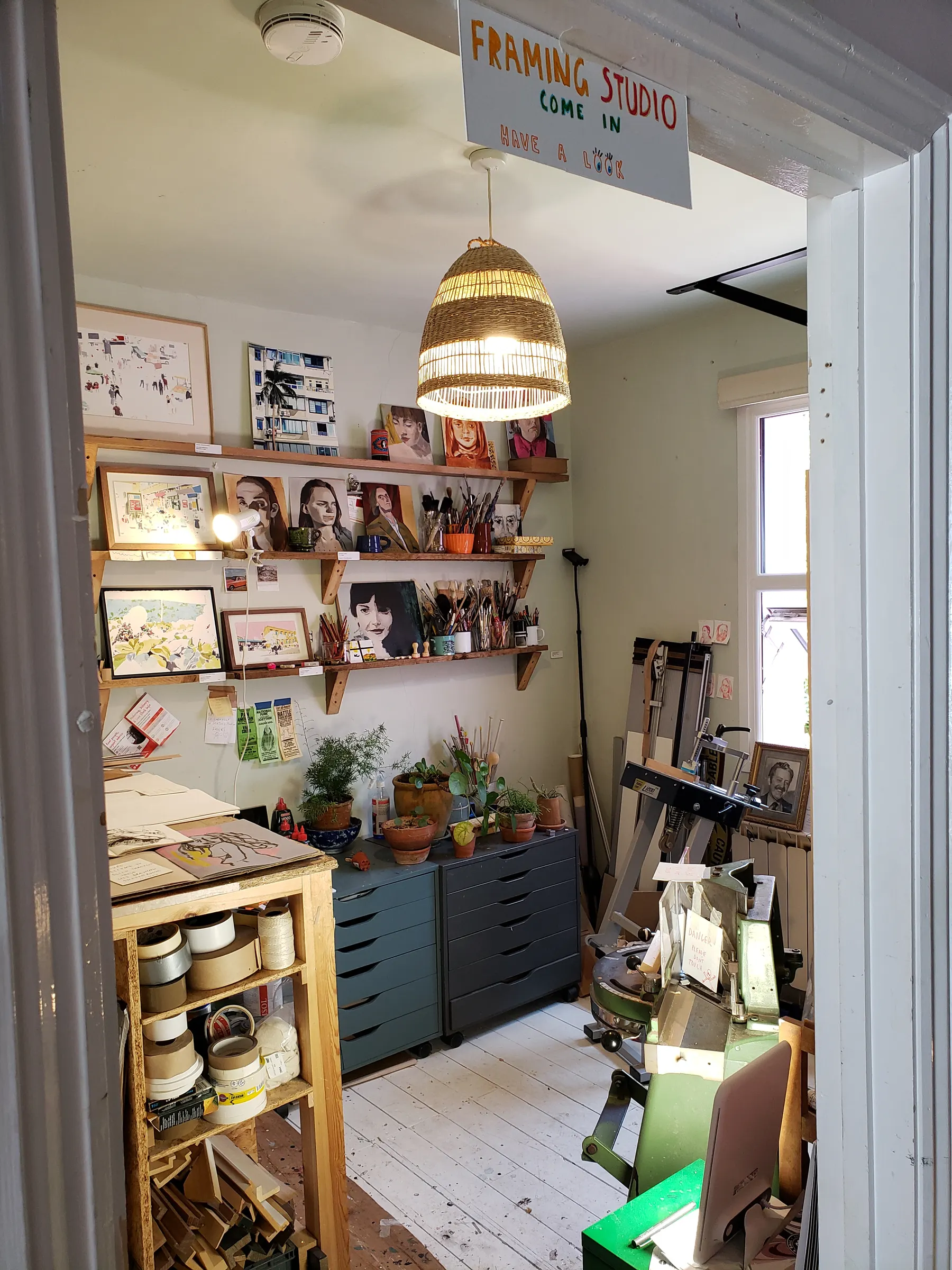 Corner of a working studio with shelves of paint, framed work and a window